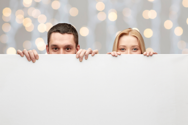 happy couple hiding behind big white blank board